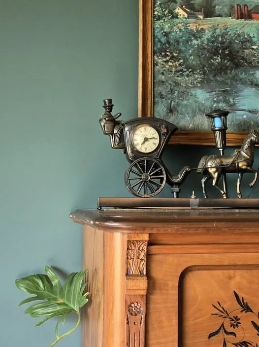 A brass carriage clock on the carved wood cabinet against the newly painted dining room wall